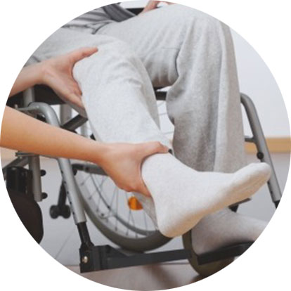 Der Patient sitzt im Rollstuhl und der Physiotherapeut hebt den Fuß.